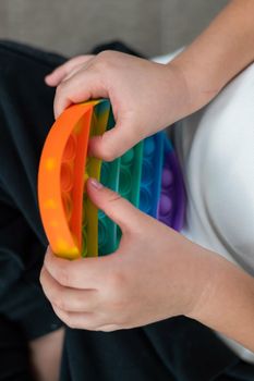 Faceless little boy playing pop it rainbow colors.