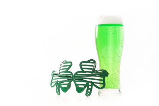 A glass of green beer and funny glasses for st patrick's day on a white background. Traditional Irish drink for a holiday. Copy spase.