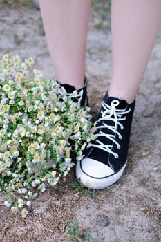 unrecognizable womens legs in sneakers near and white wildflowers outdoors on nature background on summertime