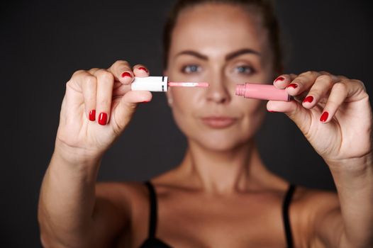 Moisturizing pink liquid lip balm gloss in the hands of a blurred beautiful Caucasian blonde woman