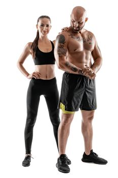 Athletic man in black shorts and sneakers with brunette woman in leggings and top posing isolated on white background. Fitness couple, gym concept.
