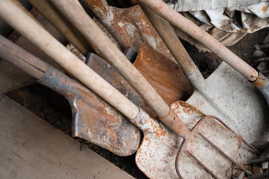 Rusted garden tools lie in a warehouse. Shovels and pitchforks
