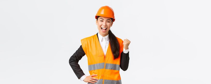 Successful businesswoman, construction manager in safety helmet, fist pump and say yes. Female asian architect celebrating great news, achieve goal at building zone, white background