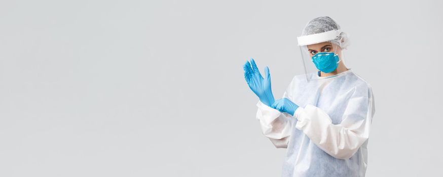 Covid-19, preventing virus, health, healthcare workers and quarantine concept. Determined young woman doctor, nurse in PPE protective equipment, face mask put on rubber gloves, working on vaccine.