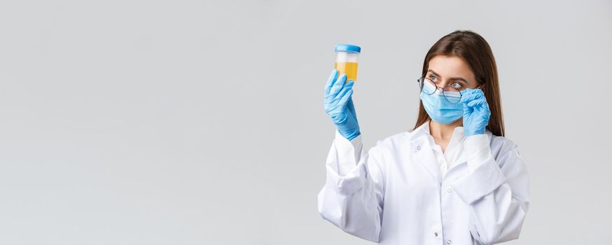 Covid-19, medical research, diagnosis, healthcare workers and quarantine concept. Professional doctor in scrubs, medical mask and gloves, looking at patient urine sample, making tests.