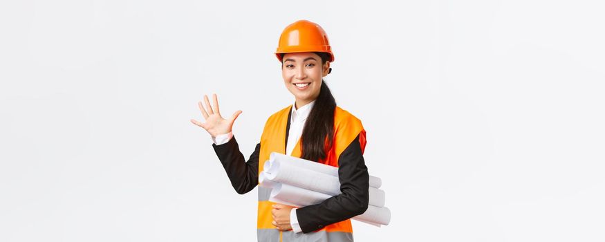 Smiling professional asian female engineer, architect giving five month for construction, carry blueprint of project and looking at camera, guarantee finish work in time, white background