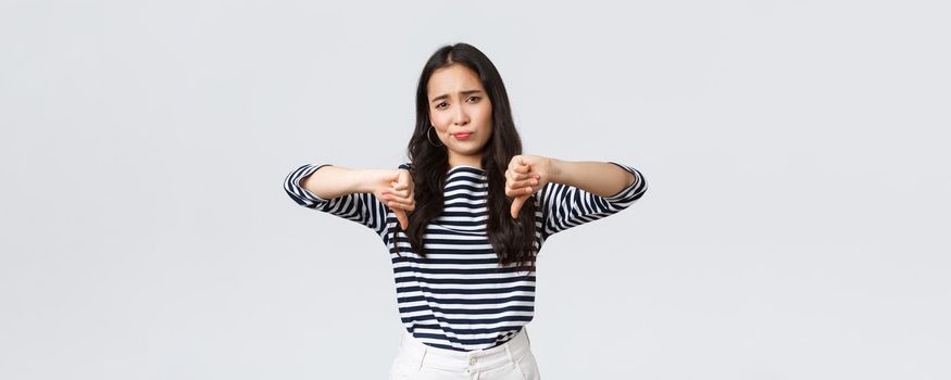 Lifestyle, beauty and fashion, people emotions concept. Judgemental disappointed asian woman showing negative opinion, make thumbs-down and smirk unsatisfied, rating bad product.