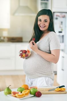 Healthy eating equals a healthy baby. Shot of a pregnant woman making a fruit salad in her kitchen.