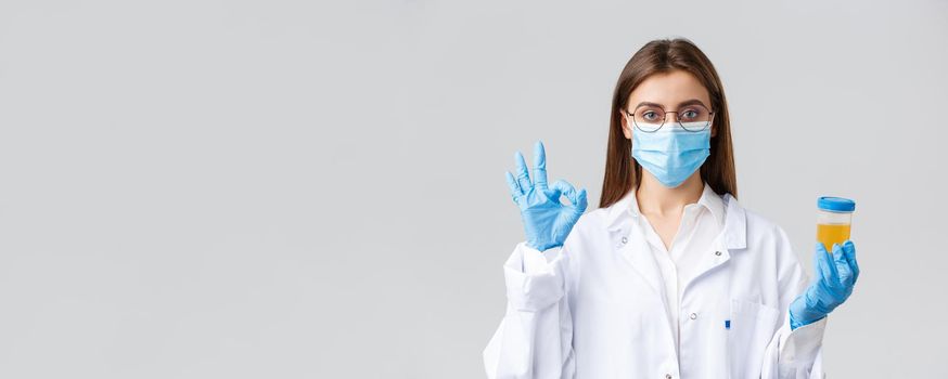 Covid-19, medical research, healthcare workers and quarantine concept. Professional doctor in scrubs, medical mask and gloves, holding patient urine sample and show okay sign, approve, making tests.