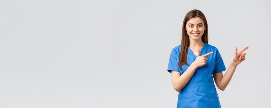 Healthcare workers, prevent virus, insurance and medicine concept. Smiling nurse or female doctor in blue scrubs, pointing fingers down, inform about coronavirus news, show information