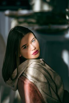 portrait of beautiful gentle woman in a beige sports jacket in the sunshine. Black long hair. sensuality and tenderness.