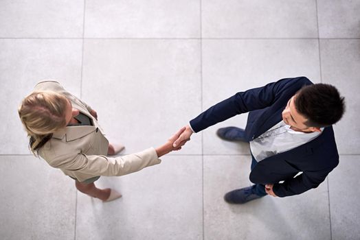 Welcome to the company. High angle shot of two professional businesspeople shaking hands in the office.