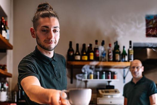 Young waiter serving a cup of coffee on a bar counter. worker serving a coffee to a customer