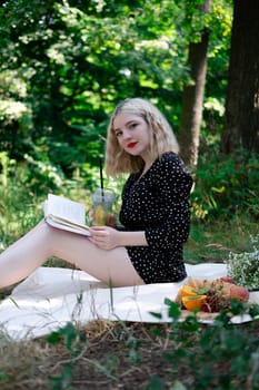 charming blonde young woman on a picnic on plaid in park with tasty snacks. Lemonade, fruits and croissants. summertime, rest, relax, enjoy. freedom