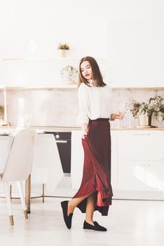 Portrait of fashionable woman in a red skirt, white blouse and stylish suede shoes with a buckle posing on the kitchen.