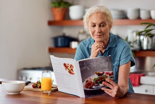 The healthy way is the smart way. Shot of a mature woman reading a book while preparing breakfast at home.
