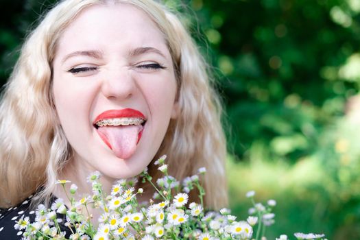 portrait of a charming blonde teenage girl wearing teeth braces with bouquet of white wildflowers. female with braces in mouth. healthy teeth. orthodontist dentist