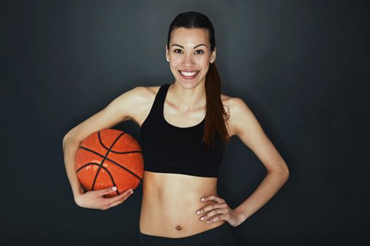 I play hard. Studio shot of a young woman holding a basketball against a dark background.