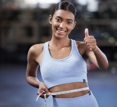 Do your best and the results will show. Portrait of a sporty young woman showing thumbs up while measuring her waist in a gym.