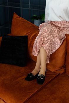 Photo of a womens legs in suede high-heeled shoes with a buckle. Posing on a sofa