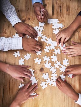 This team isnt easily puzzled. High angle shot of a group of unidentifiable businesspeople building a puzzle together in the office.