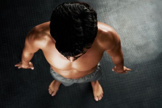 Ripped and ready. High angle shot of a muscular young man standing on a gray floor.