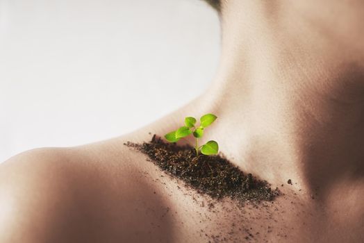 Every flower must grow through dirt. Shot of an unidentifiable young womans shoulder with soil and a small seedling on it.