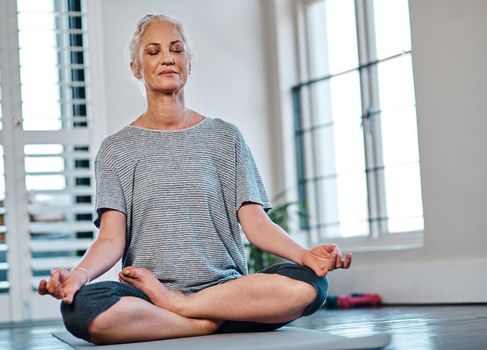 Shot of a cheerful mature woman practicing yoga while meditating inside of a studio during the day.