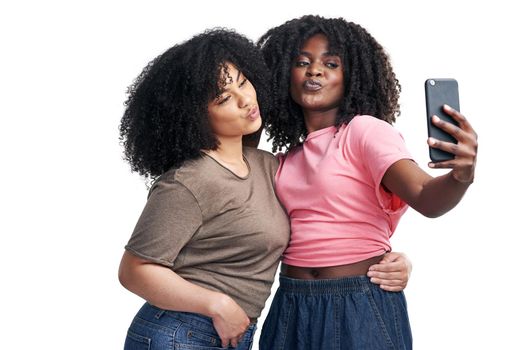 Studio shot of two young women using a smartphone to take selfies against a white background.