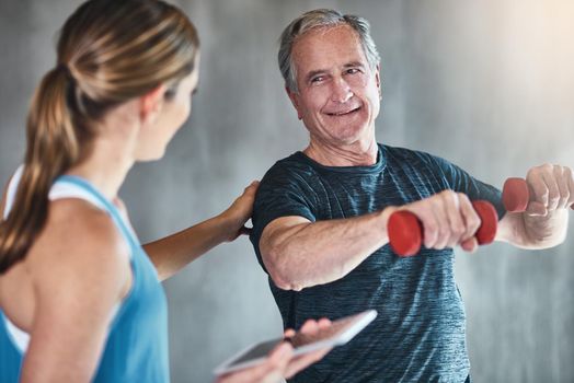 Getting older, getting fitter, getting stronger. Shot of a senior man using weights with the help of a physical therapist.