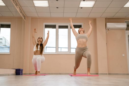 Two beautiful women do yoga, sports in the gym. The concept of grace and beauty of the body.