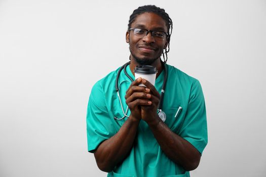 Tired african american male doctor holding cup of coffee over white background