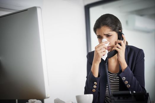 Tissues are so useful in these times. Shot of a young businesswoman making a call while blowing her nose and working in the office.