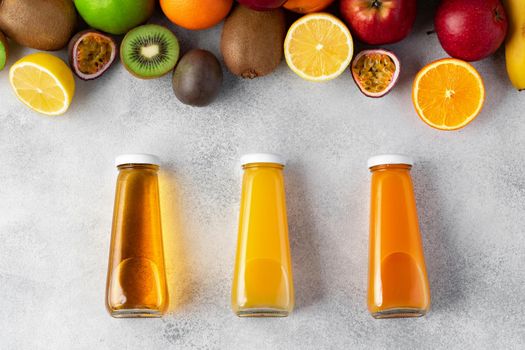 Various fruits and freshly squeezed fruits juice in bottle on gray background