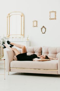 Photo of a women's legs in black high-heeled shoes with a buckle. Woman posing on a sofa
