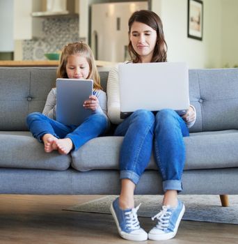 Shot of a young mother and daughter using a laptop and digital tablet on the couch at home.