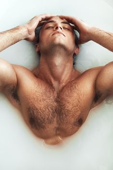 Let the milkiness submerge you. High angle shot of a handsome young man lying in a bathtub full of milky water at home.