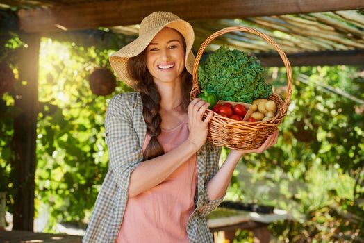 Healthy living starts in the garden. Portrait of a young woman carrying a basket of freshly picked produce in a garden.