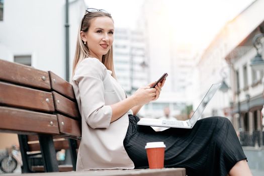 business woman with a laptop and a takeaway coffee sitting on a bench.