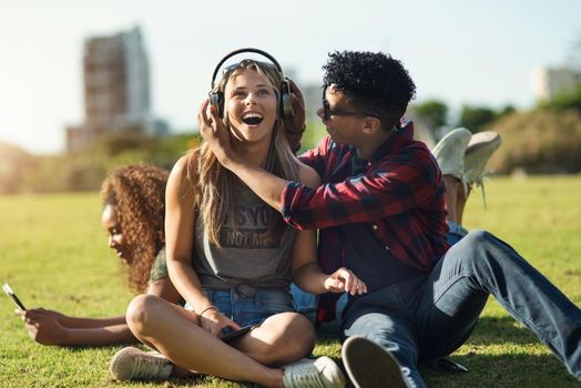 Shot of a two cheerful young friends listening to music on headphones outside on a park during the day.