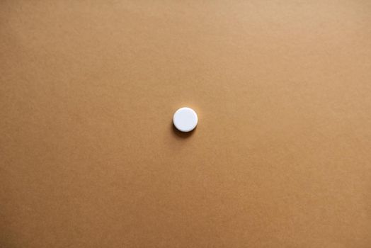 One pill makes all the difference. Studio shot of a single white tablet against a brown background.