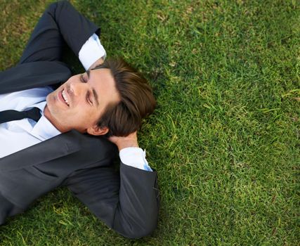 Just taking a breather. A young businessman lying down on green grass.