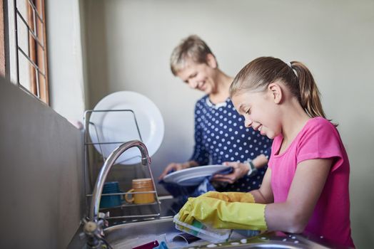 Shot of a mother and daughter cleaning dishes together.