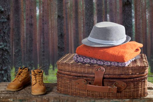 Suitcase with warm clothes and boots on wooden surface of bench