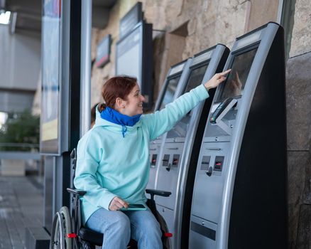 Caucasian woman in a wheelchair buys a train ticket at a self-service checkout.