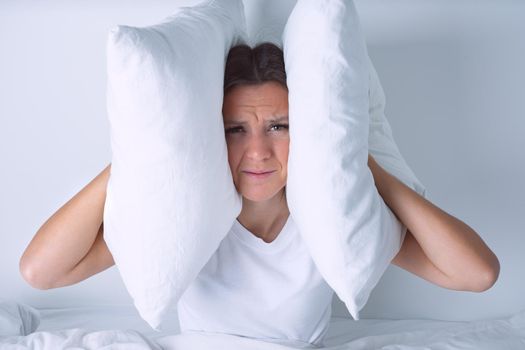 Young woman disturbed by noisy neighbours. Woman struggling from noise in bed and covering ears with pillows