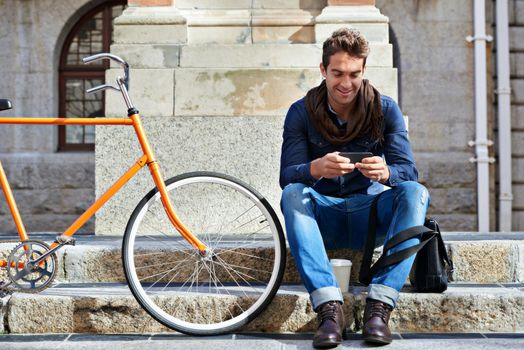 Chilling in the city. Shot of a man using his cellphone while taking a break in the city with his bicycle beside him.