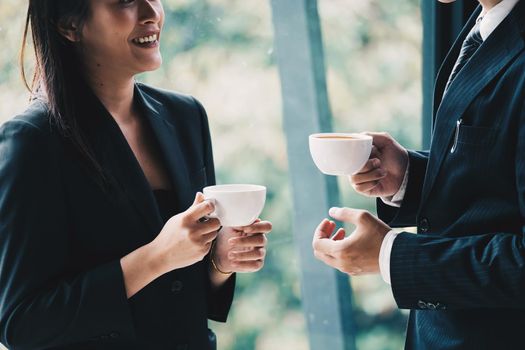 Coffee break. Group business people, standing in modern office, holding a cups, smiling standing at the window