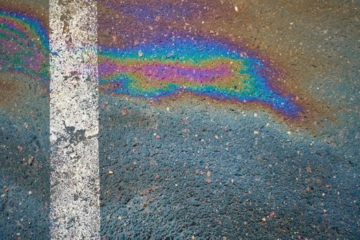 Gasoline spill on asphalt with a white dividing strip in a car park as a texture or background.