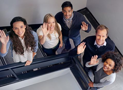 Theyre a friendly team. Business colleagues standing on the stairs waving.